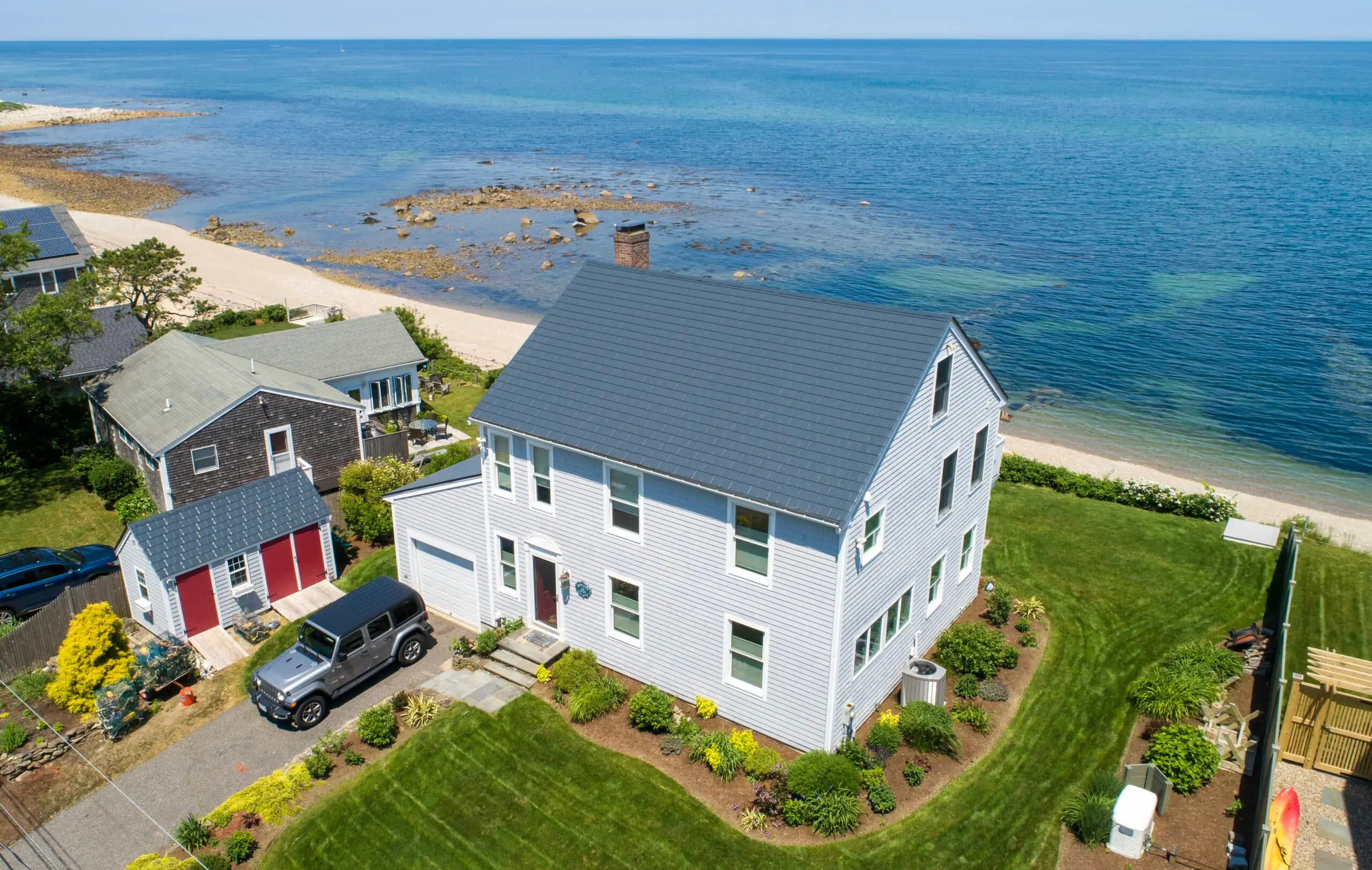 Deep Charcoal slate metal roof on a coastal home in Plymouth, Massachusetts, overlooking the Atlantic Ocean, surrounded by lush greenery and a sandy beach.