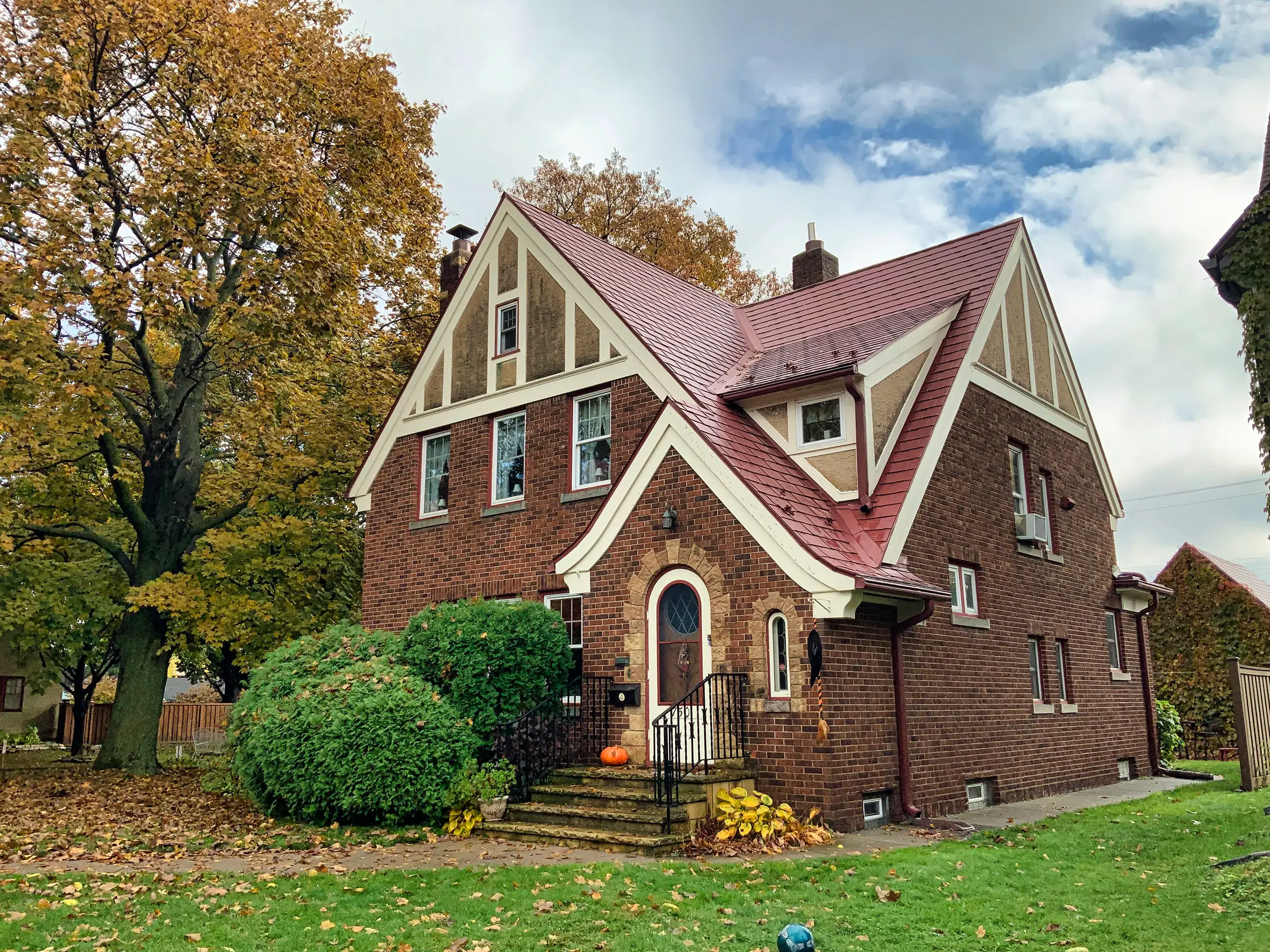 Tudor-style cottage house in St. Paul, MN, featuring a Tile Red Interlock Metal Roofing system, surrounded by autumn foliage and a well-maintained lawn.